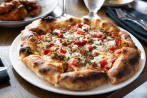 Plated pizza on a table with tomatoes, sausage, and ricotta cheese as toppings
